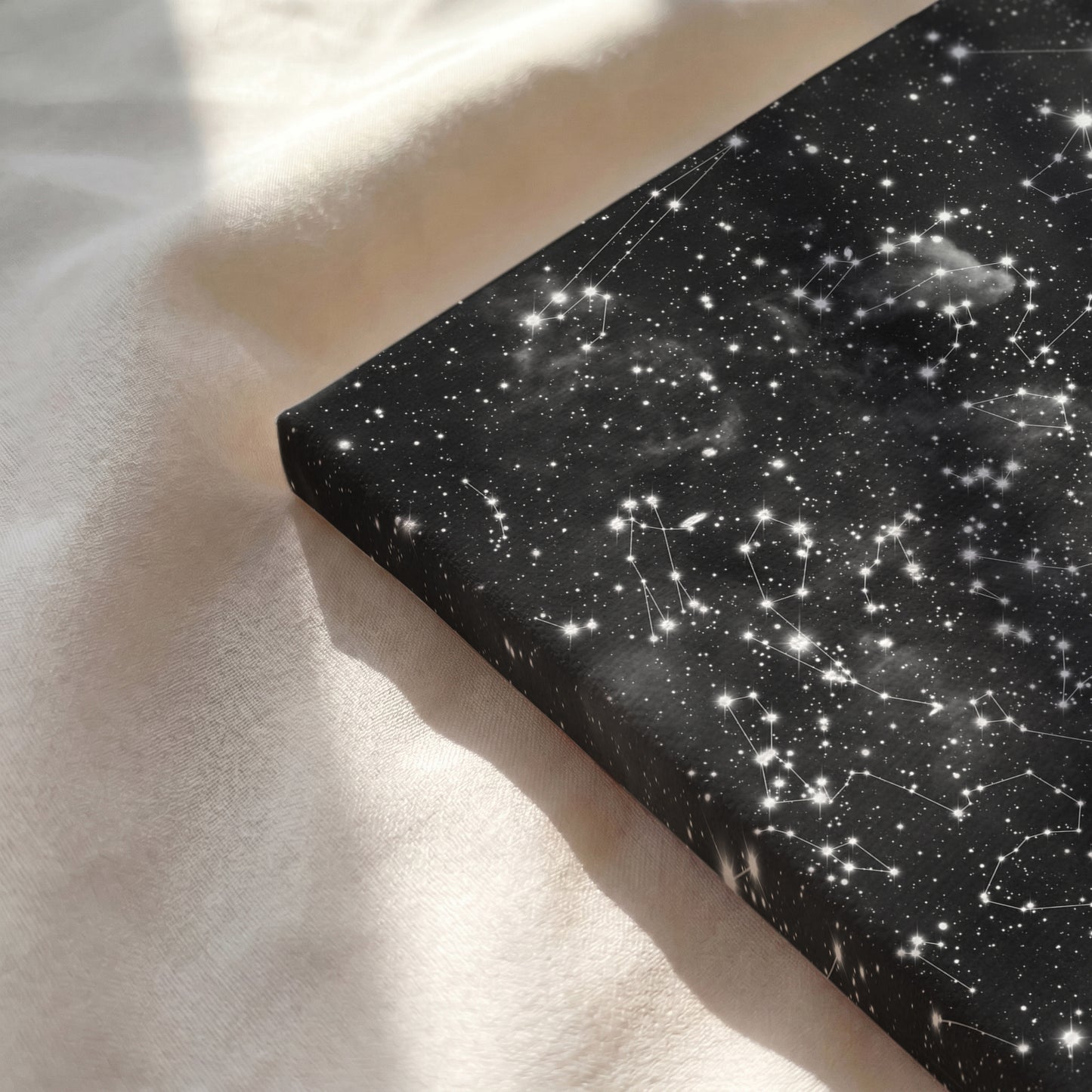 Close-up of a personalized cloud background star map printed on premium gallery-wrapped canvas resting on a soft, sunlit cream-colored fabric surface.