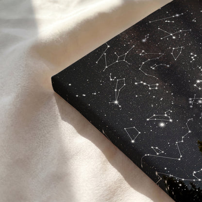 A rectangular black fabric or mat with a white constellations and star pattern, photographed on a soft cream fabric surface with natural sunlight and shadows.