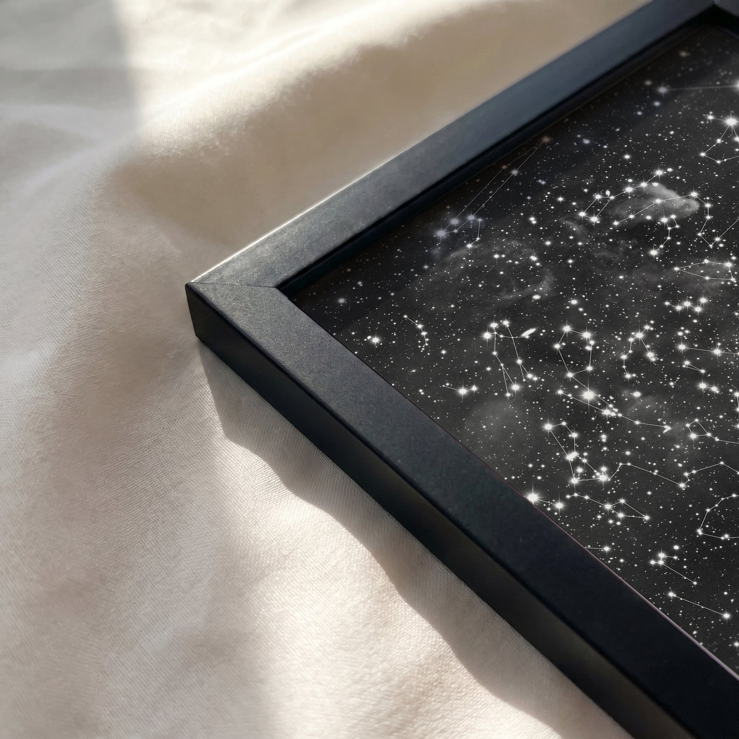 Close-up of a personalized cloud background star map print resting on a soft, sunlit cream-colored fabric surface.