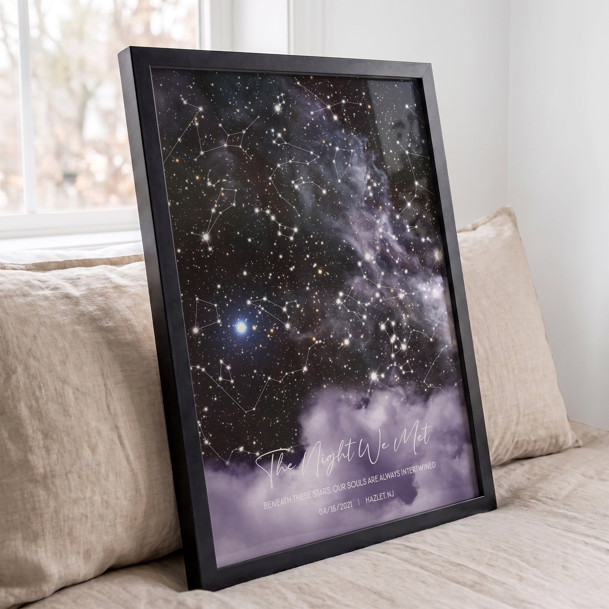 Personalized cloud background star map print leaning against a beige sofa in a bright room.