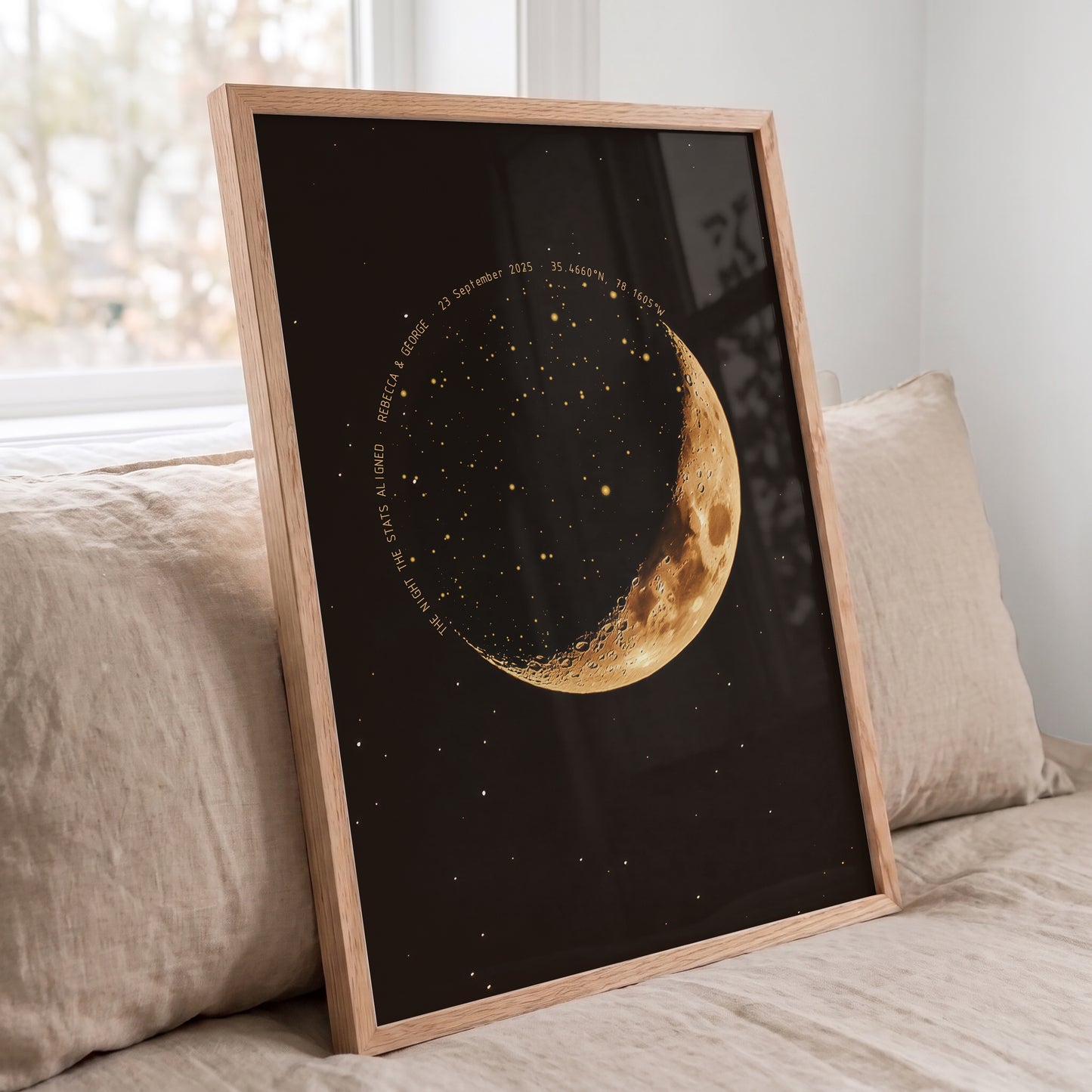 A framed art print featuring a golden crescent moon and stars on a black background, leaning against a beige sofa in a softly lit room.
