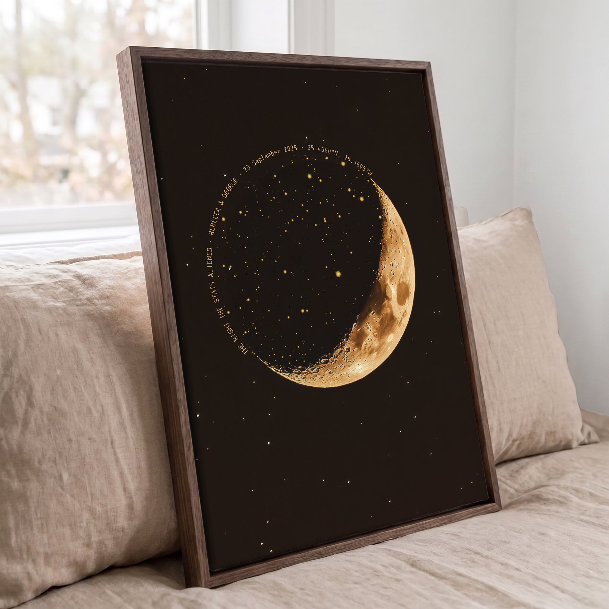Personalized moon phase star map displayed in a dark wood frame on a bed